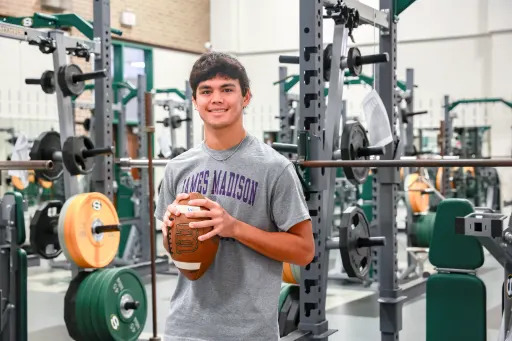 Stratford quarterback Aaron DeLeon smiles, holding a football in the weight room
