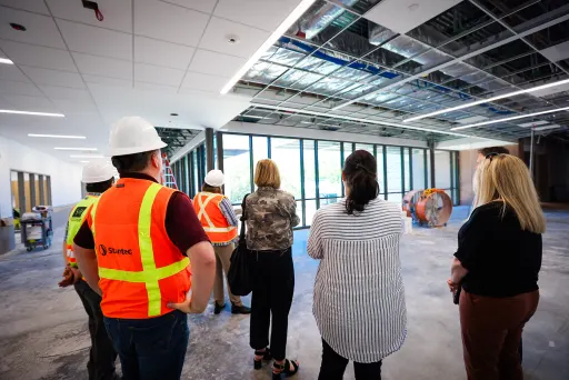 a group of people, half of them wearing high-visibility vests and hard hats, standing in a partially constructed room