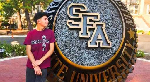 Elvis Fuentes posing in front of a sculpture of a Stephen F. Austin University class ring