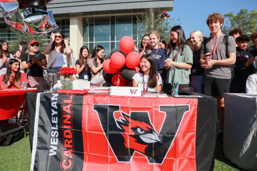 Grace Wu sitting behind a table with a Wesleyan University Cardinals flag