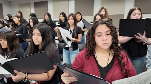 choir students with binders open, standing on risers
