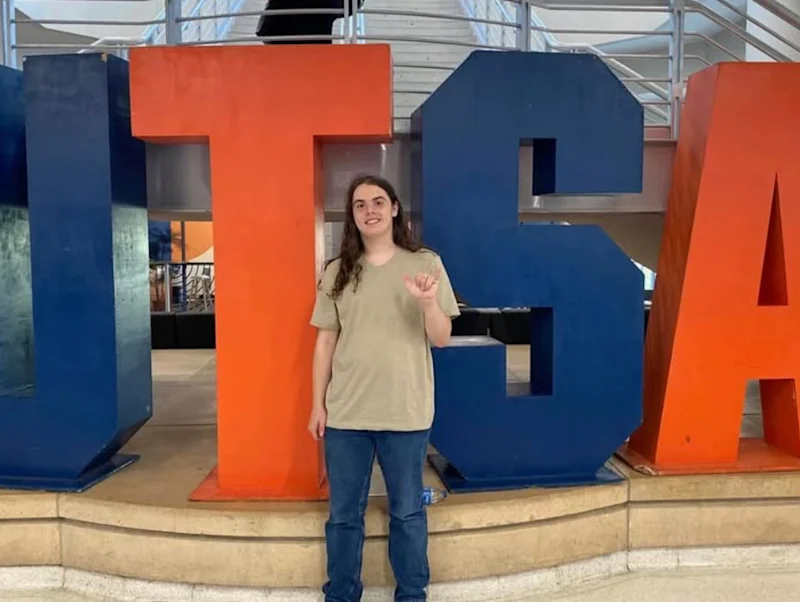 Tristan Walton in front of sign reading "U.T.S.A."
