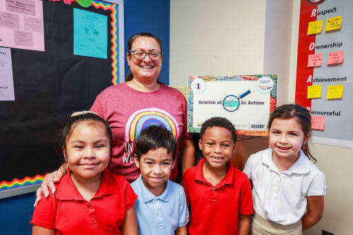 A teacher posing with four students in front of a bulletin board
