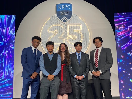 Formally-dressed students and teacher standing in front of photo backdrop reading "RBPC 2025"