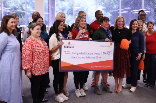 Students and teachers holding a large novelty check for $5,000 addressed to "Distinguished Scholars Winner"
