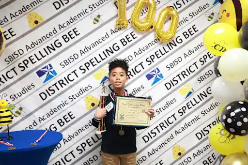 a spelling bee competitor holds his plaque and trophy
