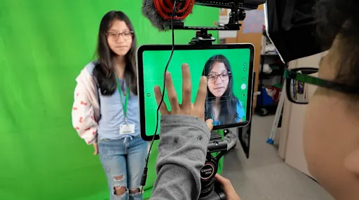 one student recording another student in front of a green screen