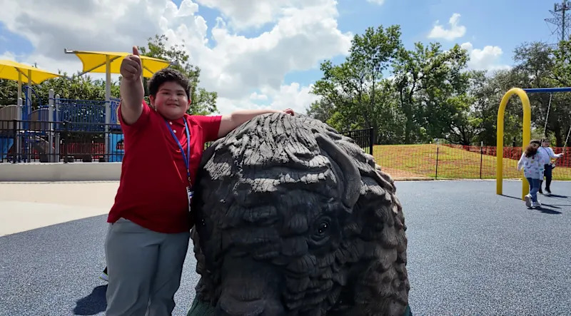 elementary school student sits next to a buffalo statute in the middle of new buffalo creek playground