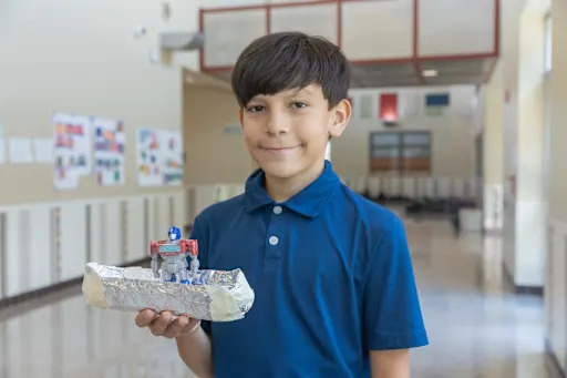 student holding up aluminum foil boat