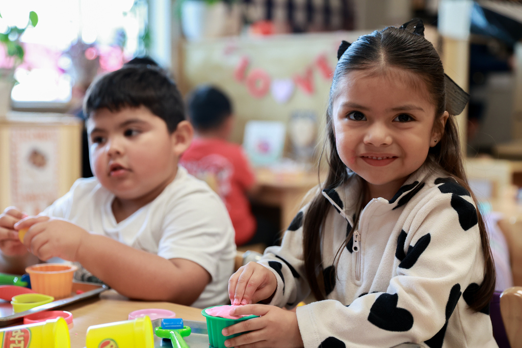 Two children seated at a table, one wearing a white shirt, the other in a cow-print long-sleeve.