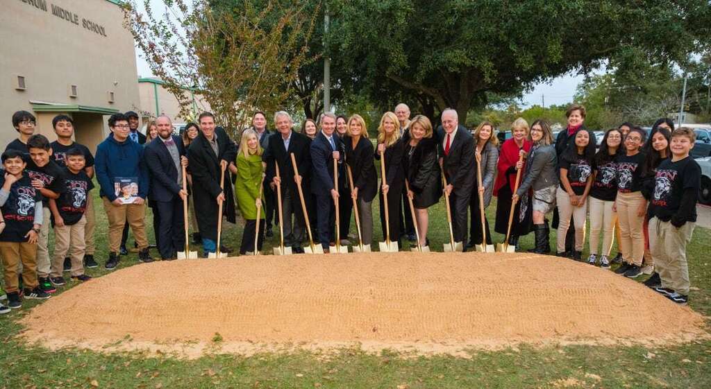 People in suits and casual clothing surround a dirt plot for a new construction project.