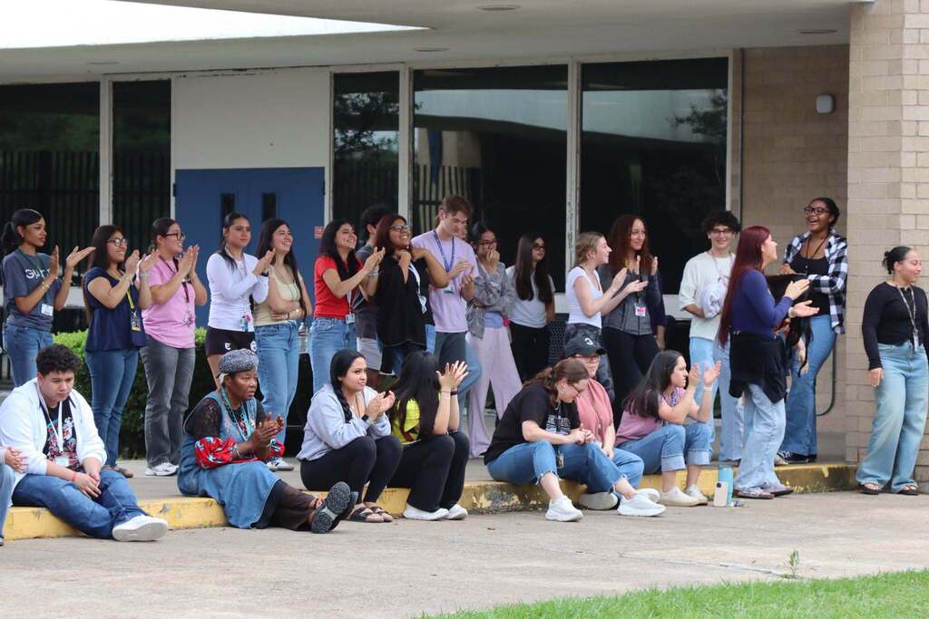 A crowd of people gathered outside a building, some standing and others seated, many holding cameras and taking pictures.