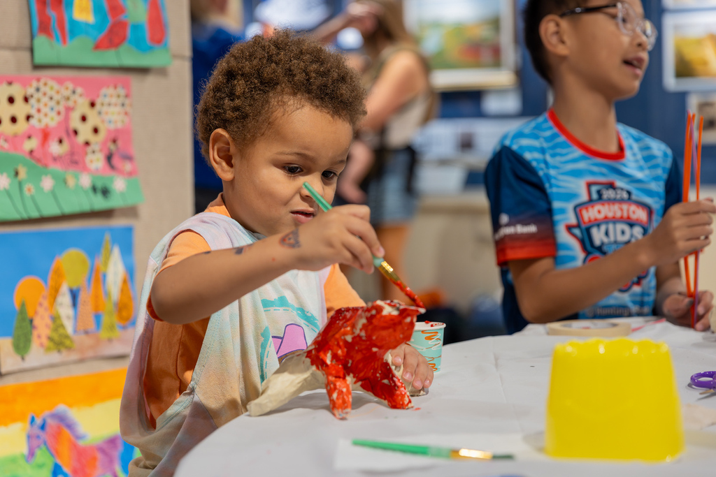 A child paints a red object while sitting at a table in a brightly decorated room.