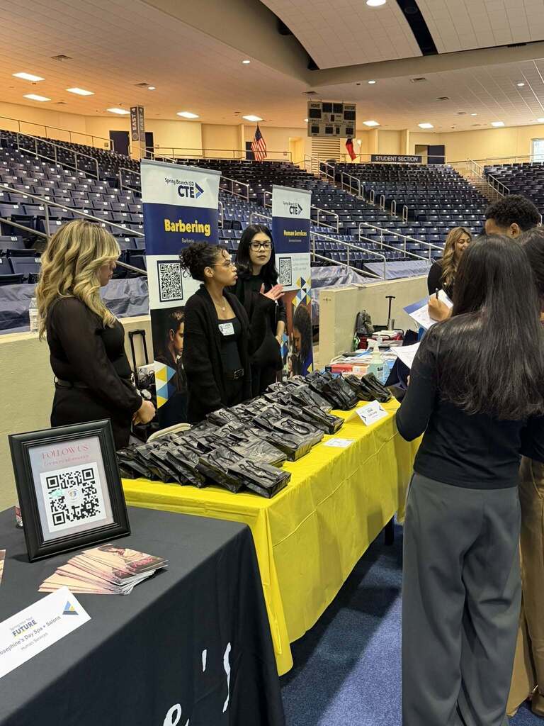 People stand around a table with yellow cloth and a QR code sign, looking at items on the table.