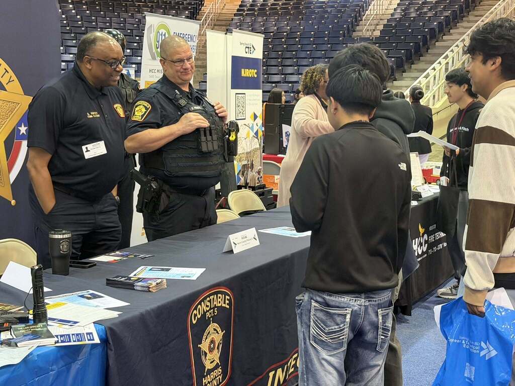 Police officers in uniform at a booth, interacting with people. Papers, a bag, and a blue tablecloth are on the table.