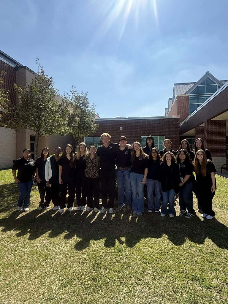 A group of people in black shirts pose for a picture on the lawn in front of a building.