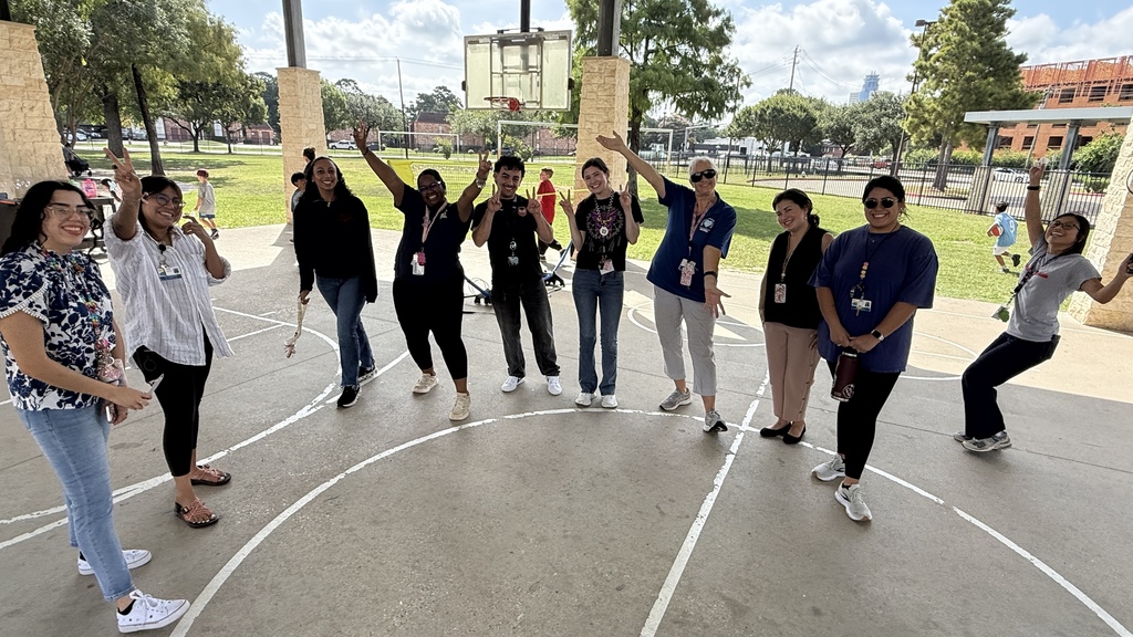 People in white shirts and dark pants stand in a circle on a basketball court with white lines.