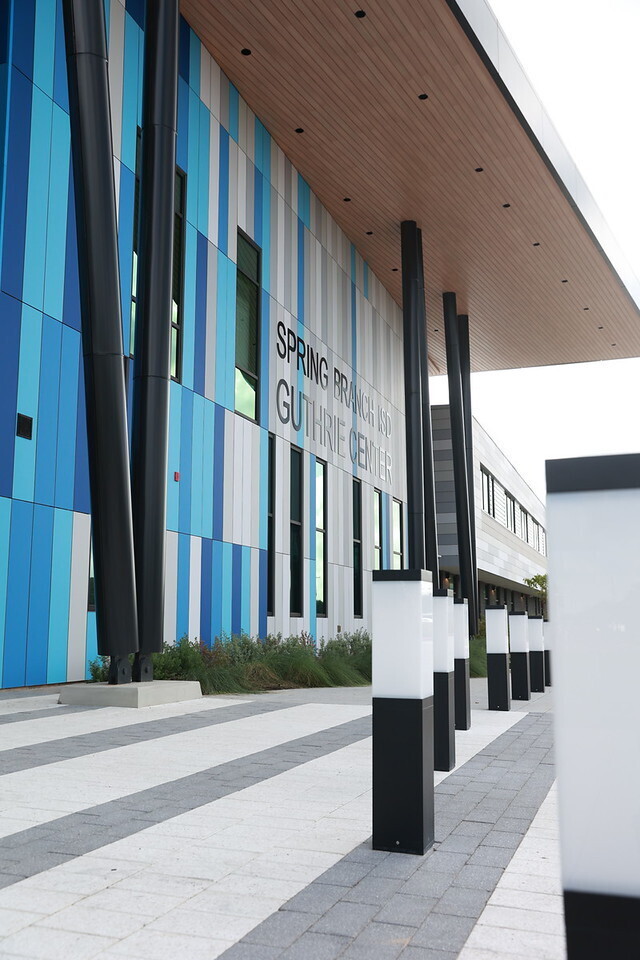 Blue and white stripes on a building. Black poles and a walkway in front. Overcast sky.