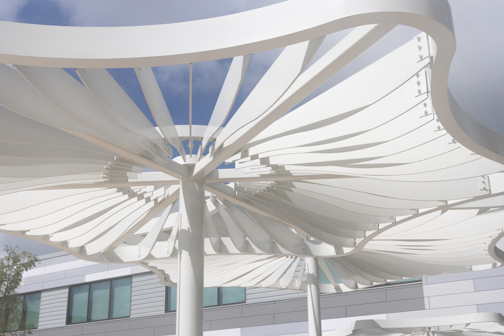 White, sunshade-like canopy above a building with windows, against a blue sky.