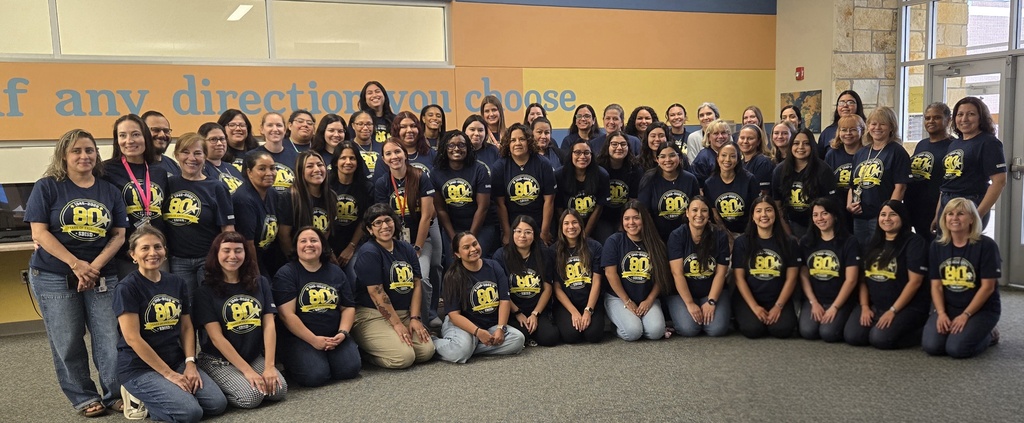 EWE faculty and staff wearing our 80th anniversary SBISD shirts pose for a picture inside a brightly lit room.