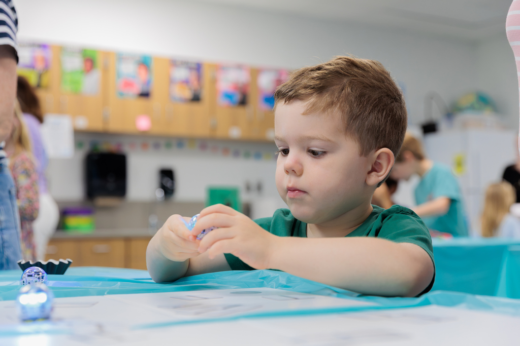 A young boy in a green shirt sits at a table and plays with a small object.