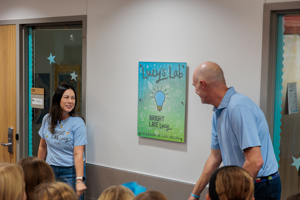 A woman and a man in light blue shirts stand before a poster. Behind them, a door with stars is visible.
