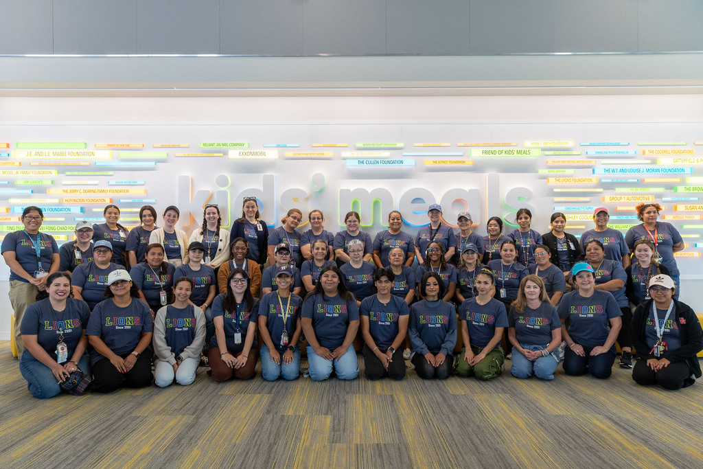 A group of people in blue shirts and casual attire pose for a photo in a room.