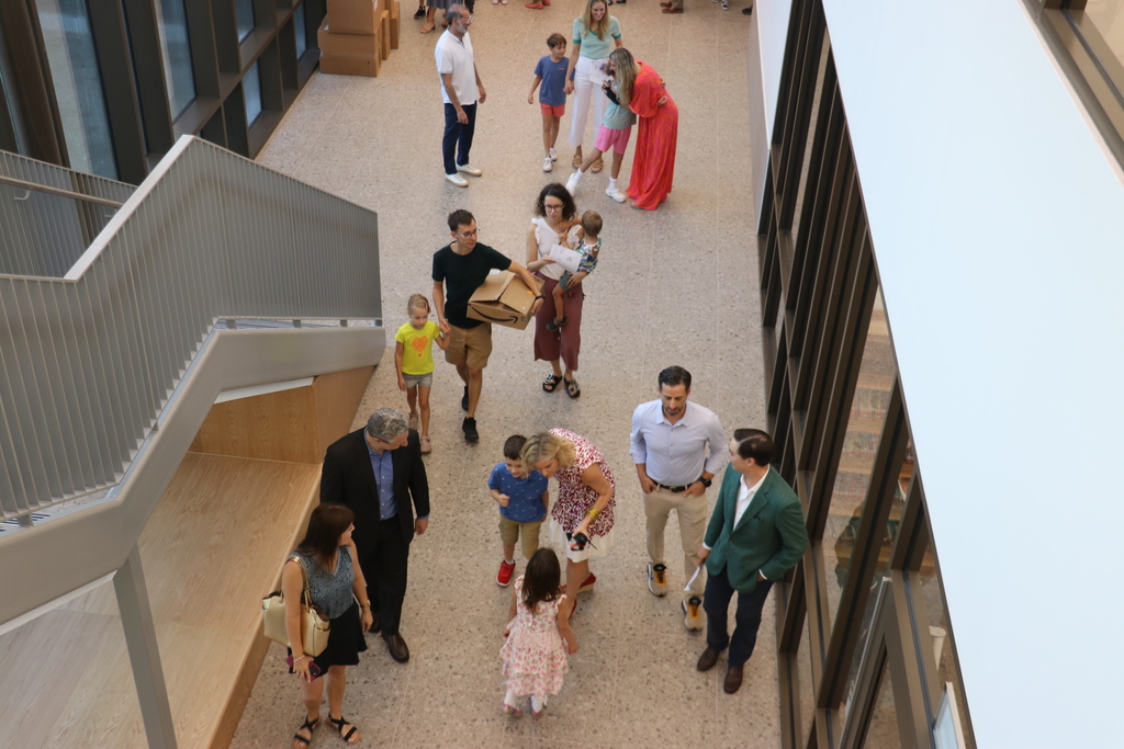 Group of people in an open area, with some walking and others standing, including a few carrying bags.