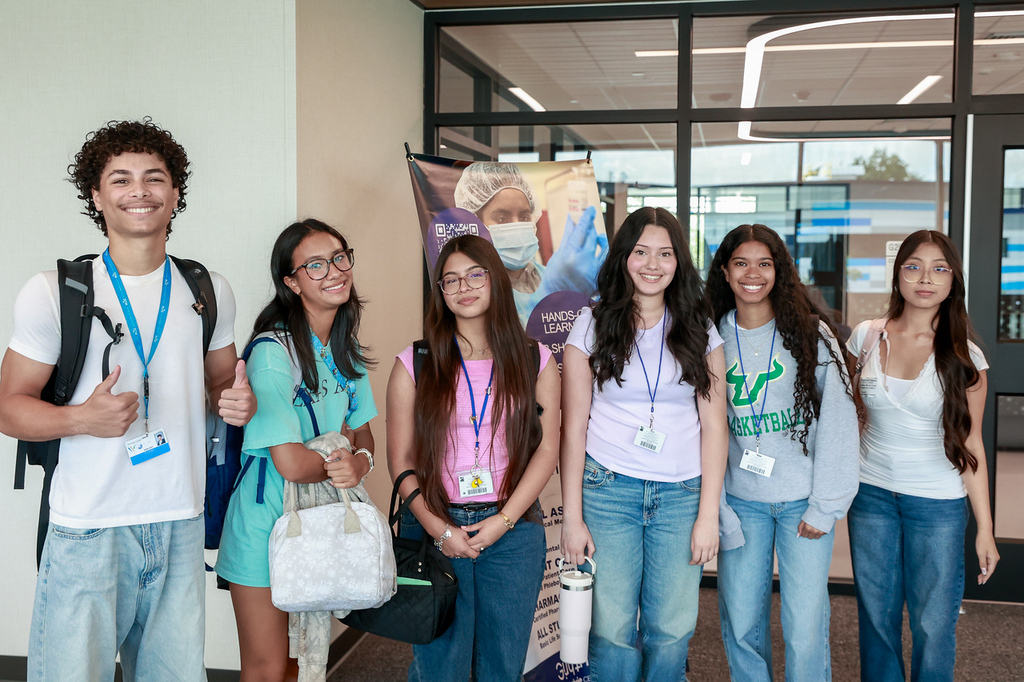 A group of young people with name tags, smiling and standing in front of a glass door.