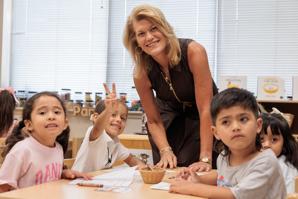 A woman in black stands behind a table with three children, one of whom gives a peace sign.