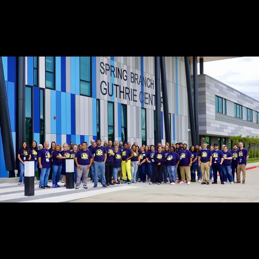 A group of people in matching blue shirts stand in front of a building named Spring Branch Guthrie Center.