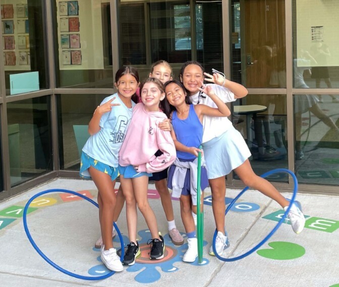 Five young girls in sports wear pose together in a brightly colored, outdoor, play area.