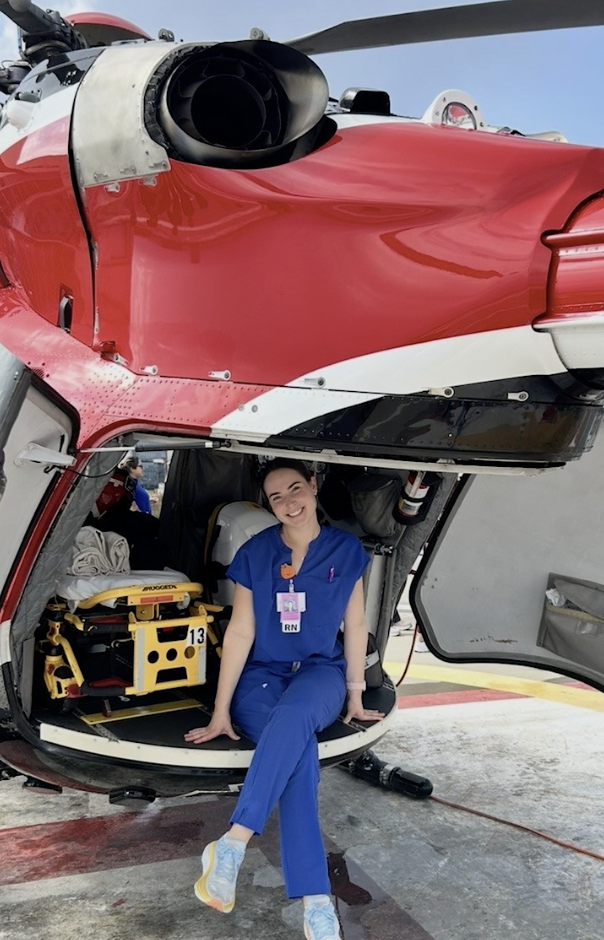 Person in blue medical attire sitting on the open door of a red helicopter with medical equipment inside.