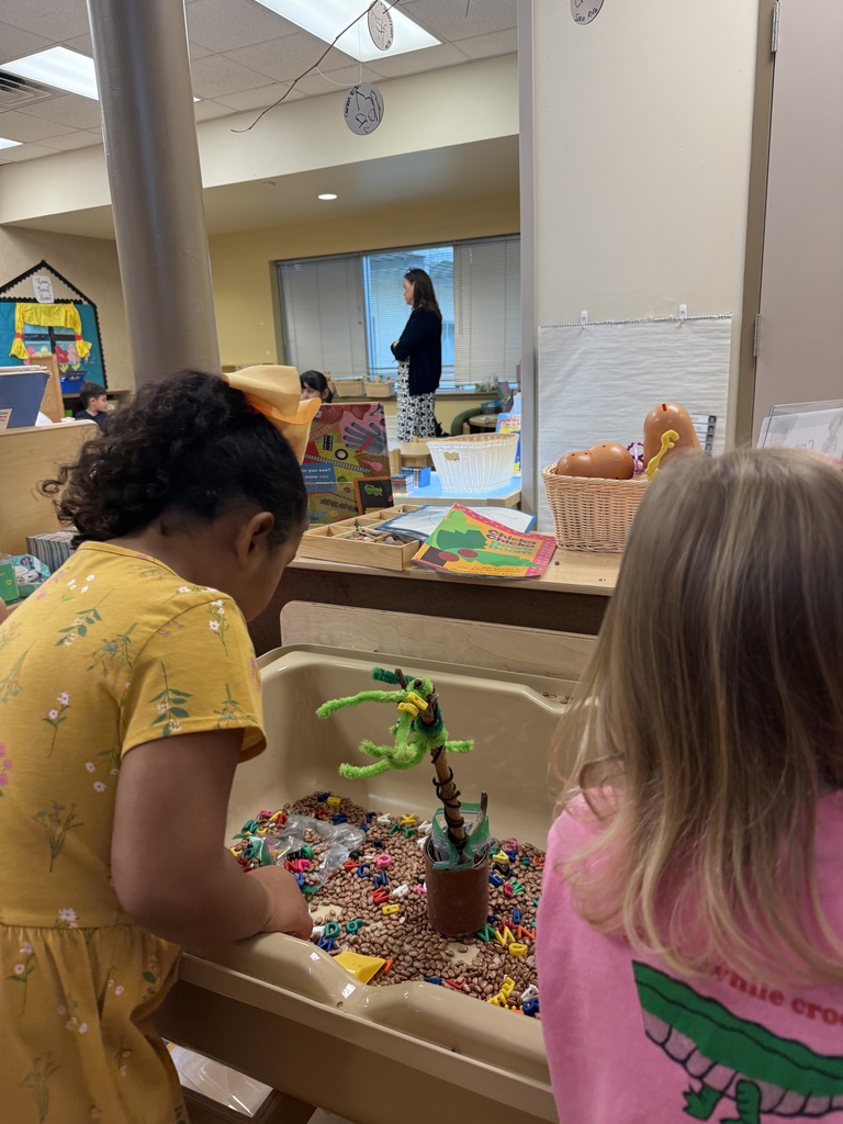 Two children play in a sensory bin with colorful objects. One child leans over the bin.