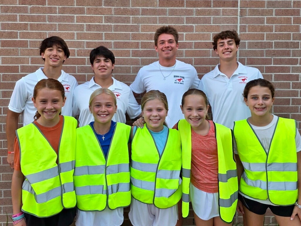 Group of children and young adults in neon safety vests pose against a brick wall.