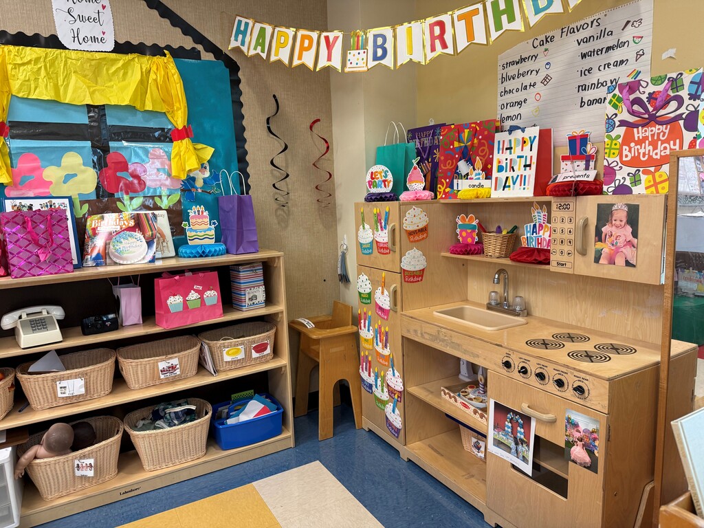 Playroom with wooden shelves. One shelf holds baskets and books. Another has toys. A birthday banner is in the background.