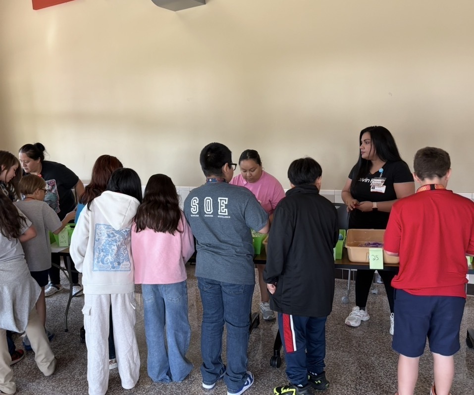 A group of people are standing in a room with tables. One woman stands at the front.
