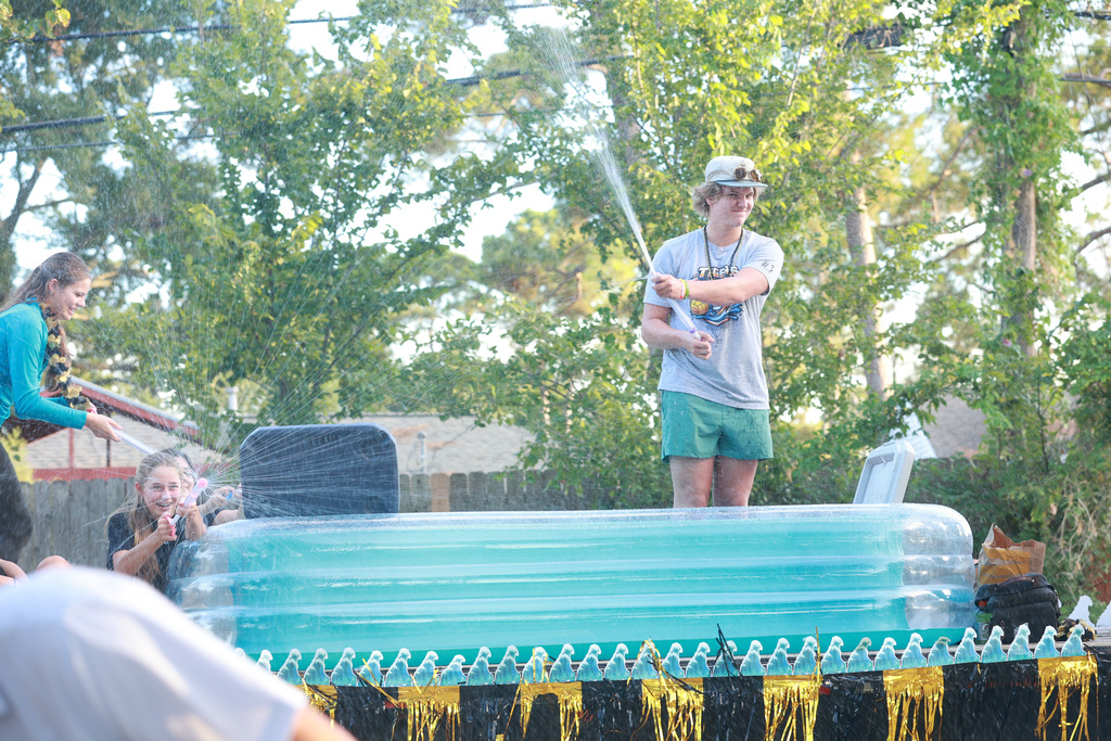 A person sprays water from a hose on a pool float while another person holds a hose.