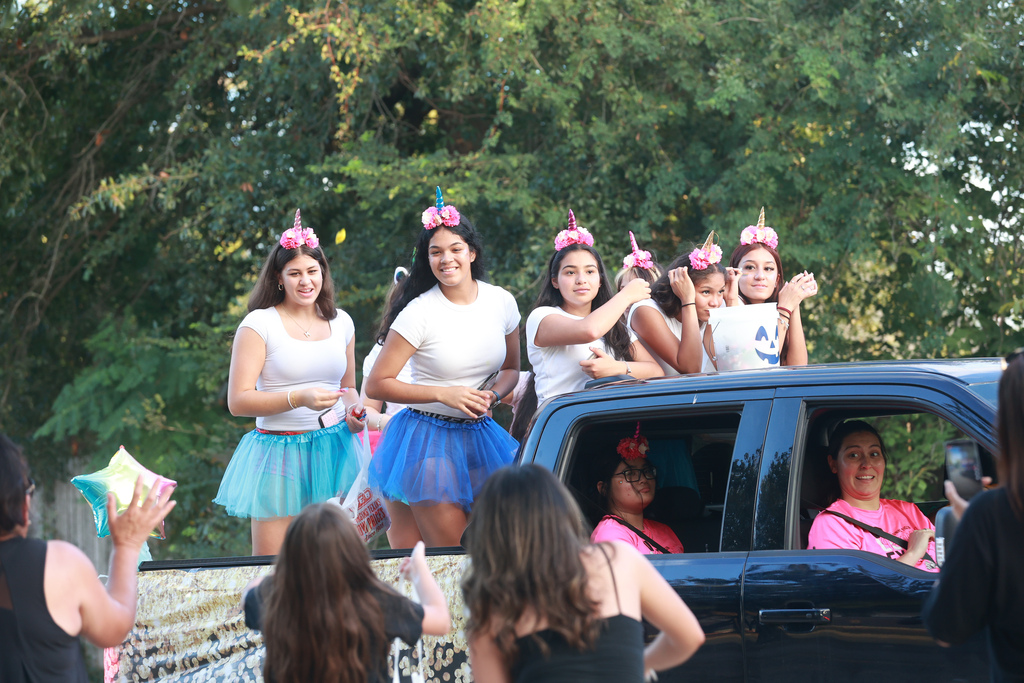 A group of women wearing white tops and tutus with pink unicorn horns on a float.