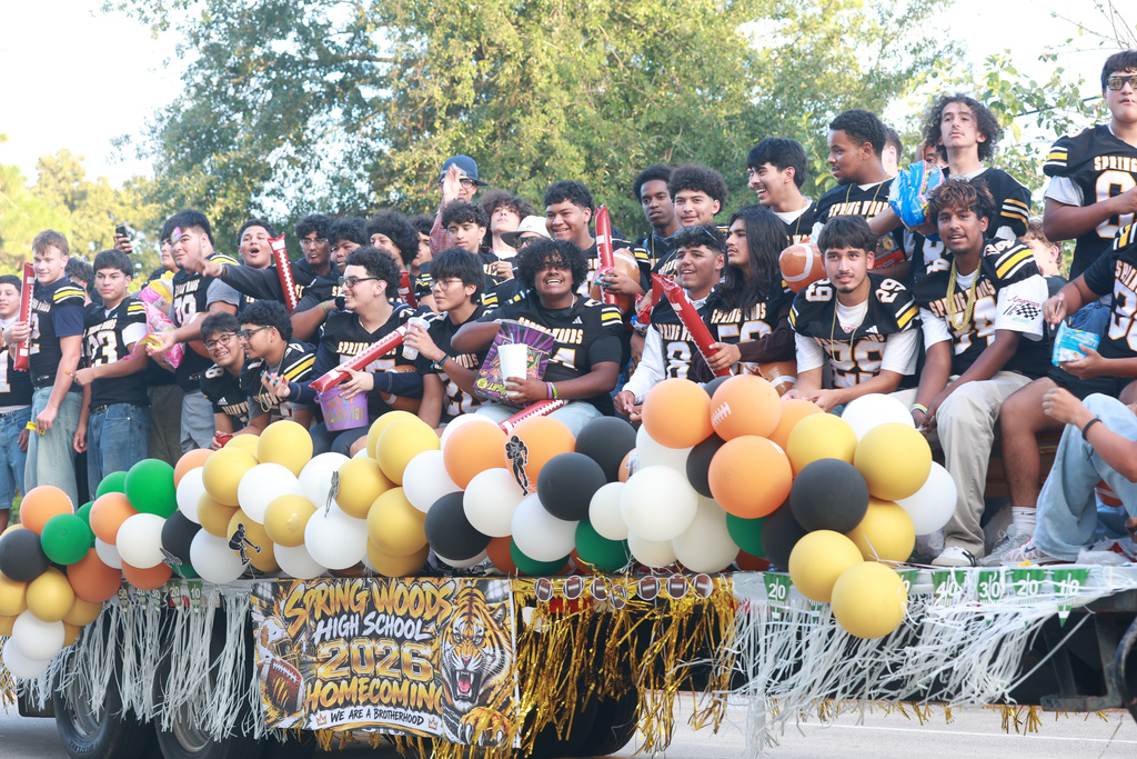 A float filled with students. Colorful balloons adorn the float. Many students wear black jerseys.