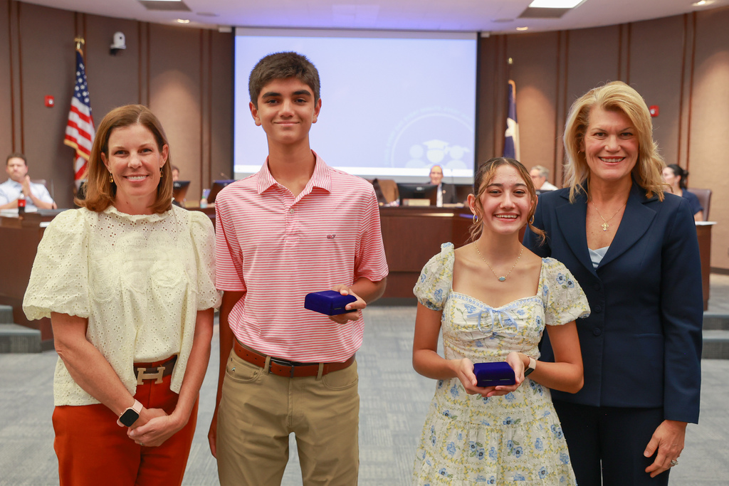 Four people stand in a conference room holding awards. Two women and a man are in the front.