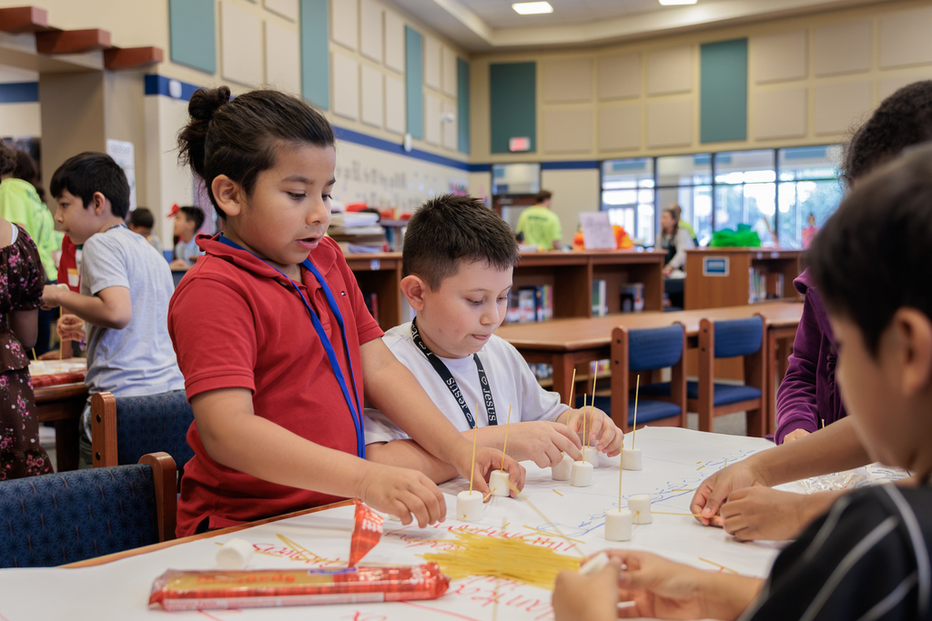 Children in a classroom, engaged in a group activity with a table full of materials.