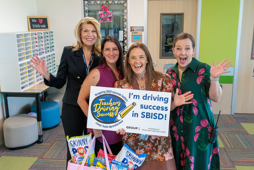 Five women stand in a room, smiling and holding a sign with "I'm driving success in SBISD!" They pose for a photo.