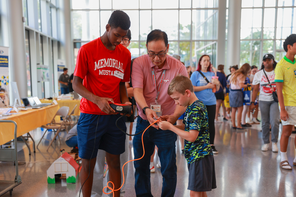 Man and boy standing in a hall, a man holds a device, and the boy holds a wire.