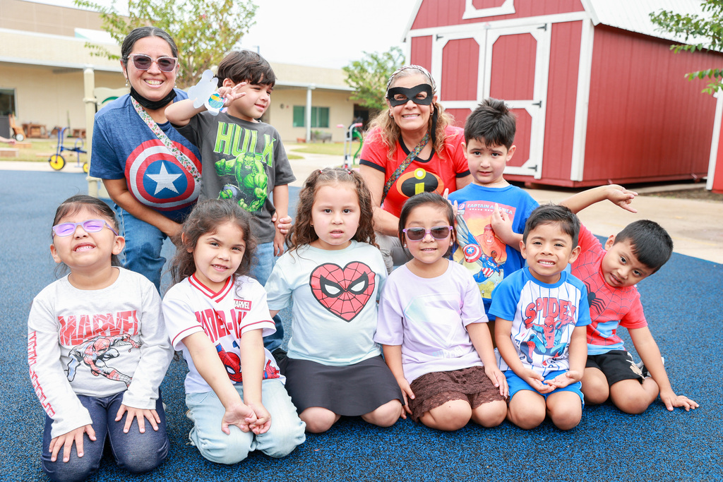 A group of children dressed in superhero costumes pose for a photo on a blue surface.