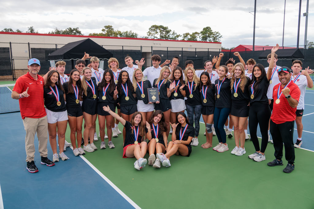 Group of tennis players on a court, standing and sitting with medals around their necks.