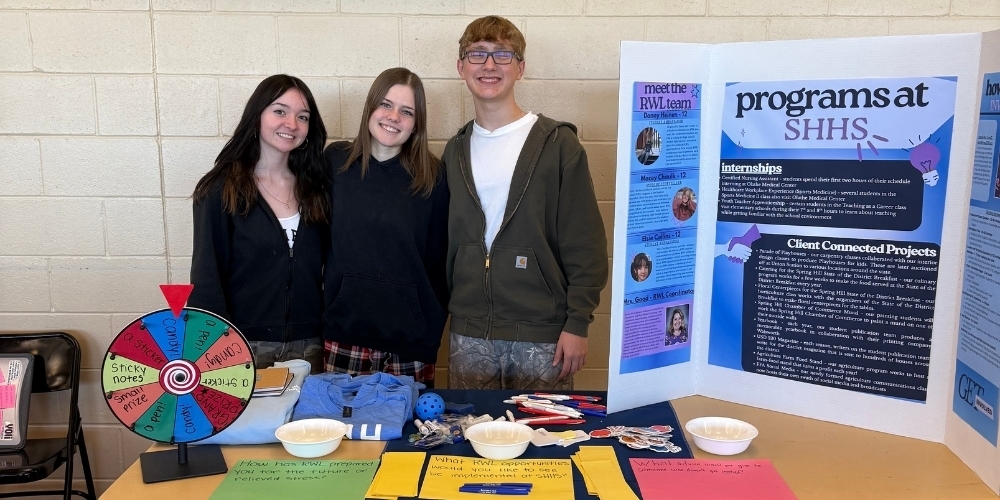 Three Spring Hill High Students posing behind a table that displays various items related to Real World Learning