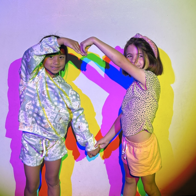 Students forming a heart in front of RGB stage lights at the Amazeum