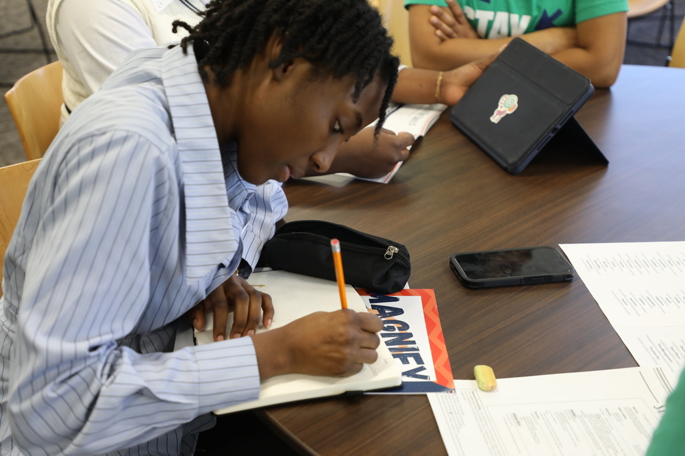 A student writes on paper during the training day for the Magnify Internship Program