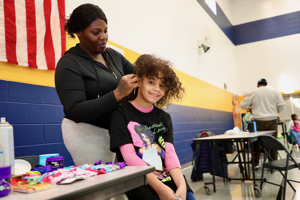 A student gets he hair braided by a volunteer hairstylist